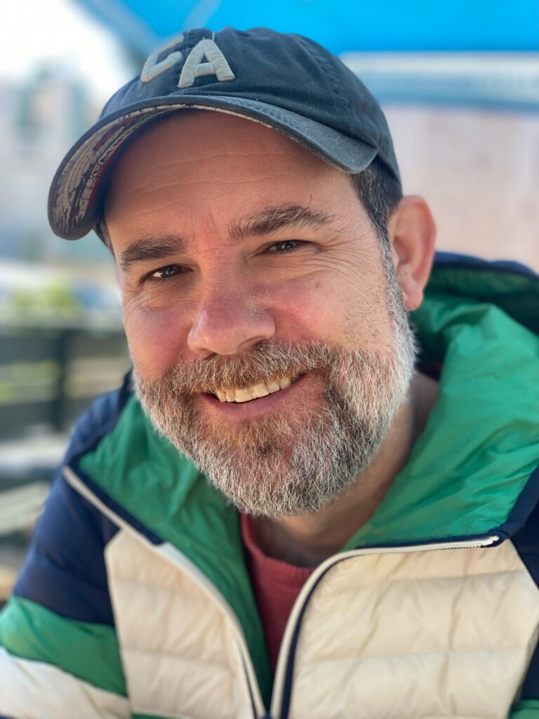 Brent Fletcher smiles wearing a cap and jacket outdoors.