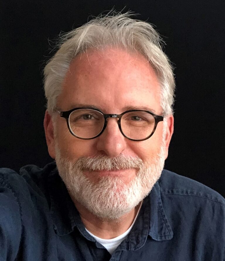 Portrait of David Crank, a man with gray hair, glasses, and a beard, smiling.