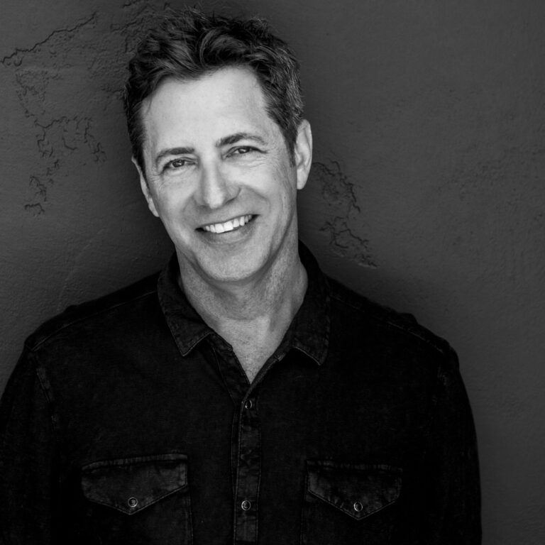 Todd Helbing portrait, smiling against a textured wall.