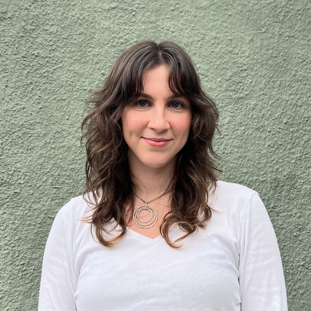 Woman with layered brown hair smiles in front of a green wall.