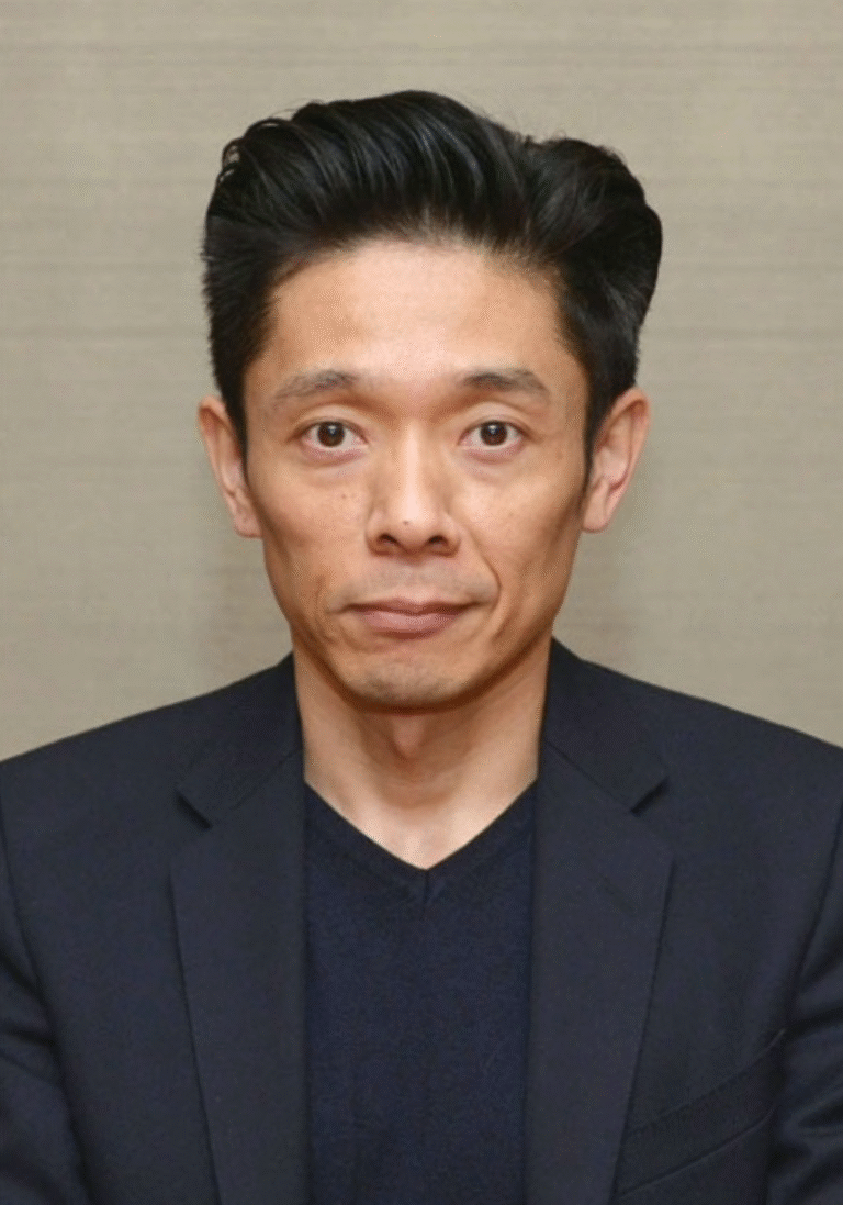 Kazu Hiro portrait wearing a dark suit and sweater.