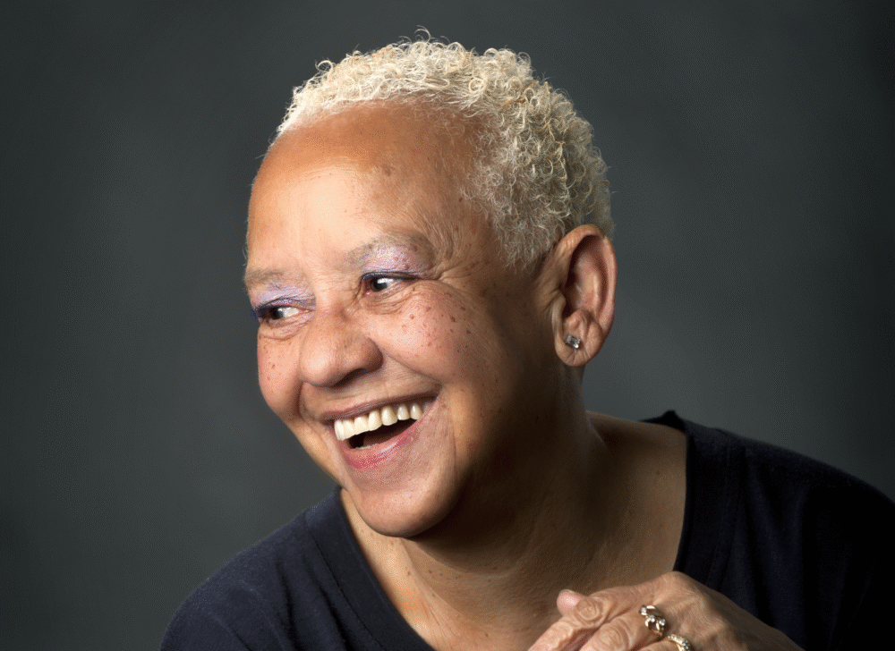 Smiling Nikki Giovanni, a Black woman with short blonde hair, wearing purple eyeshadow.