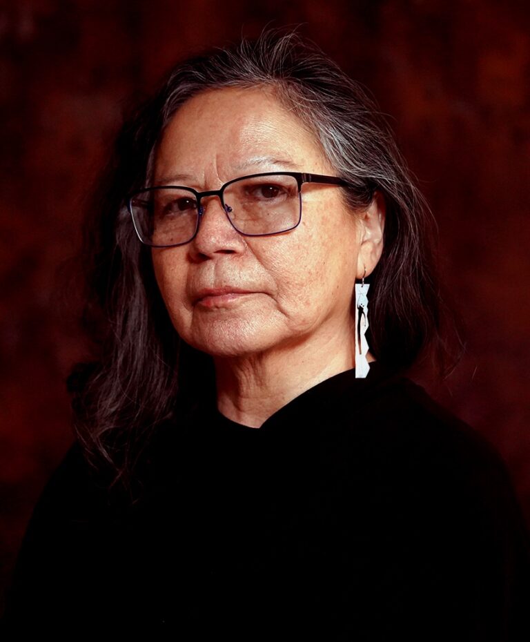 Shelley Niro portrait with glasses and artistic earrings.