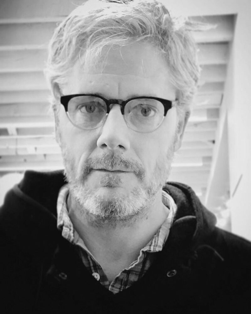 Black and white portrait of Thomas Piper with glasses and a beard.