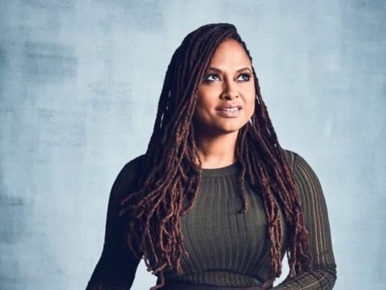 Ava DuVernay portrait with long dreadlocks, looking up against a textured blue background.
