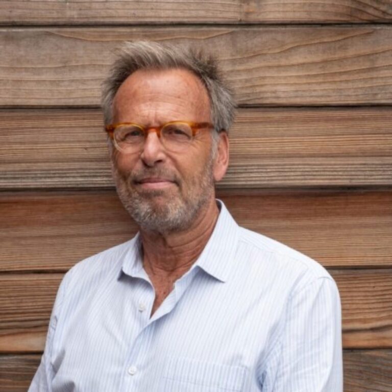Portrait of Mark Johnson, wearing glasses and a light blue shirt, against a wooden wall.
