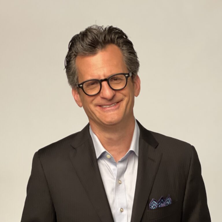 Ben Mankiewicz smiles in a suit and glasses