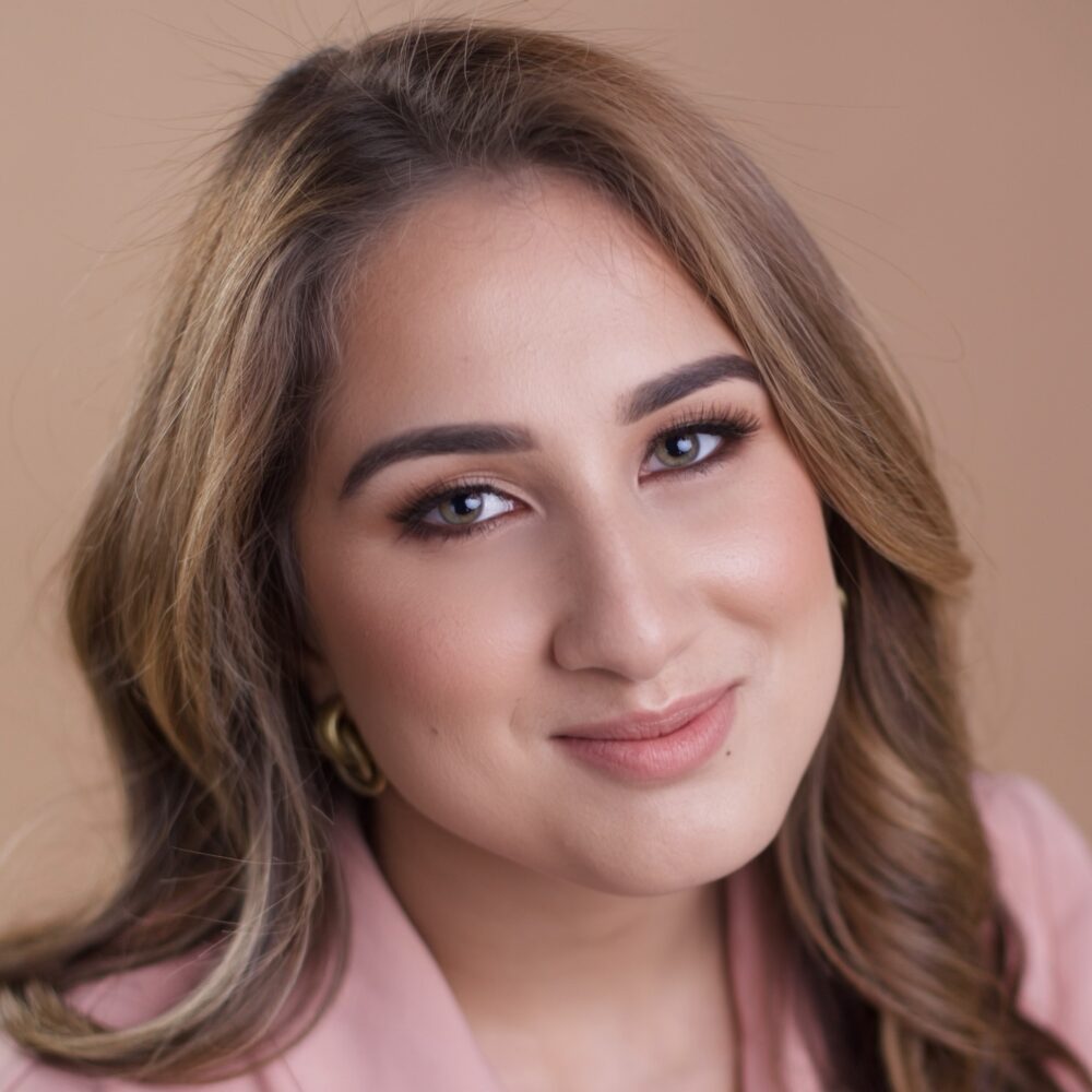 Rebe Malaret, a woman with long, wavy blonde hair, smiles warmly in a pink blazer.