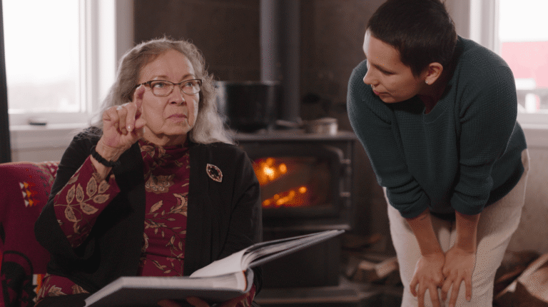 Elderly Cree woman teaching from a book to a younger person