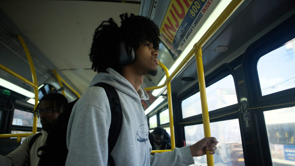 Young Black man with headphones on a bus, looking out the window