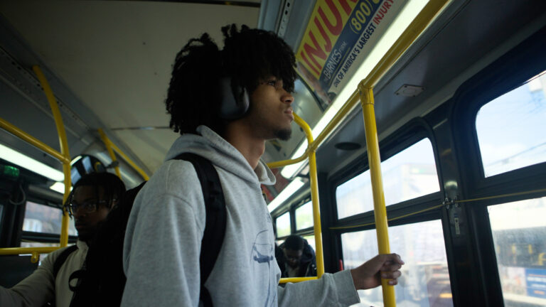 Young Black man with headphones on a bus, looking out the window