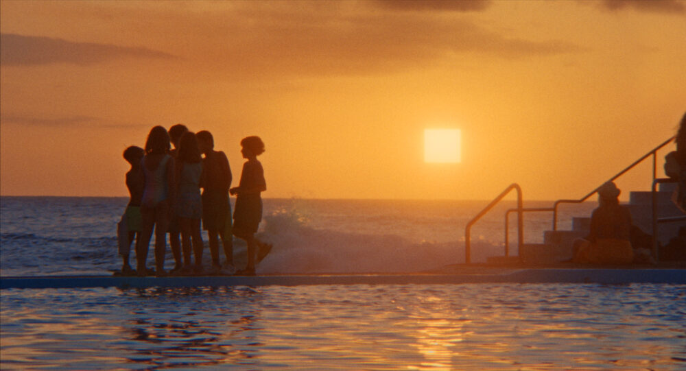 Children silhouetted at sunset by a pool, with the ocean behind them.