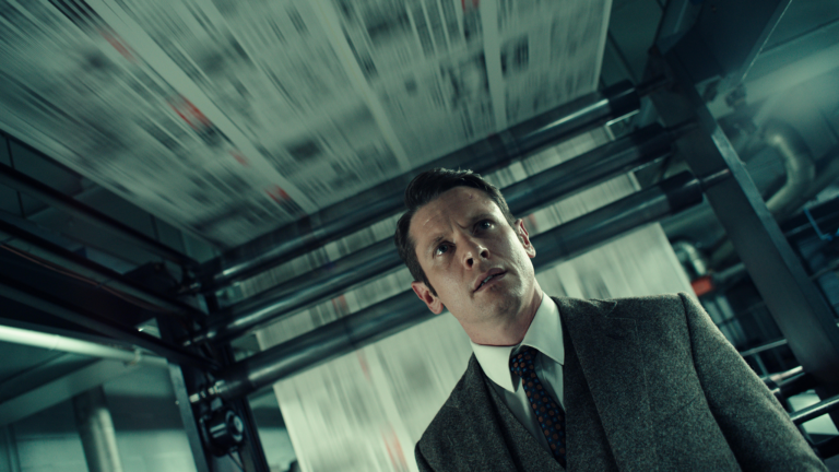 Man in suit looks up at printing press with blurred newspaper sheets