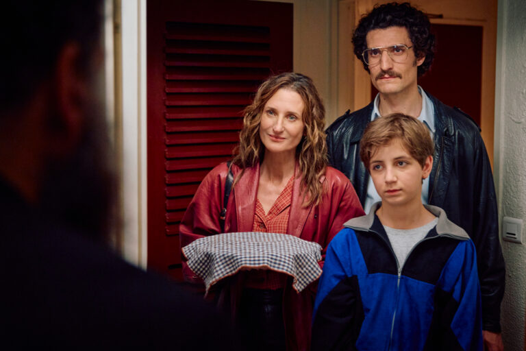 A woman shows a VHS tape labeled "Le Rêve de Laure" to four boys in a video store.