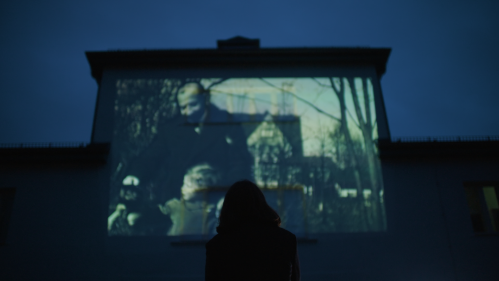 Person watches projection of old family photos on a building facade