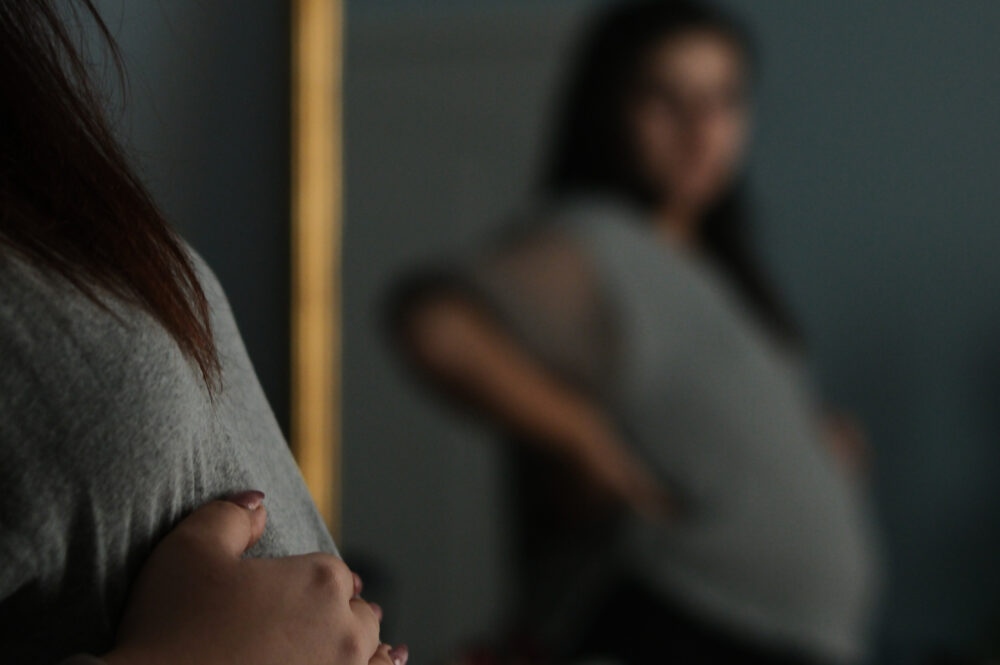 Pregnant woman looking in mirror, touching her belly.