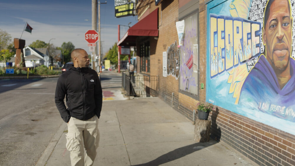 Man walks past George Floyd mural, a community canvas.