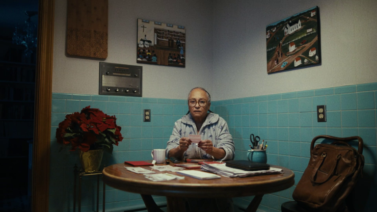 Elderly person counting cash at a table, with poinsettias and art on the wall.