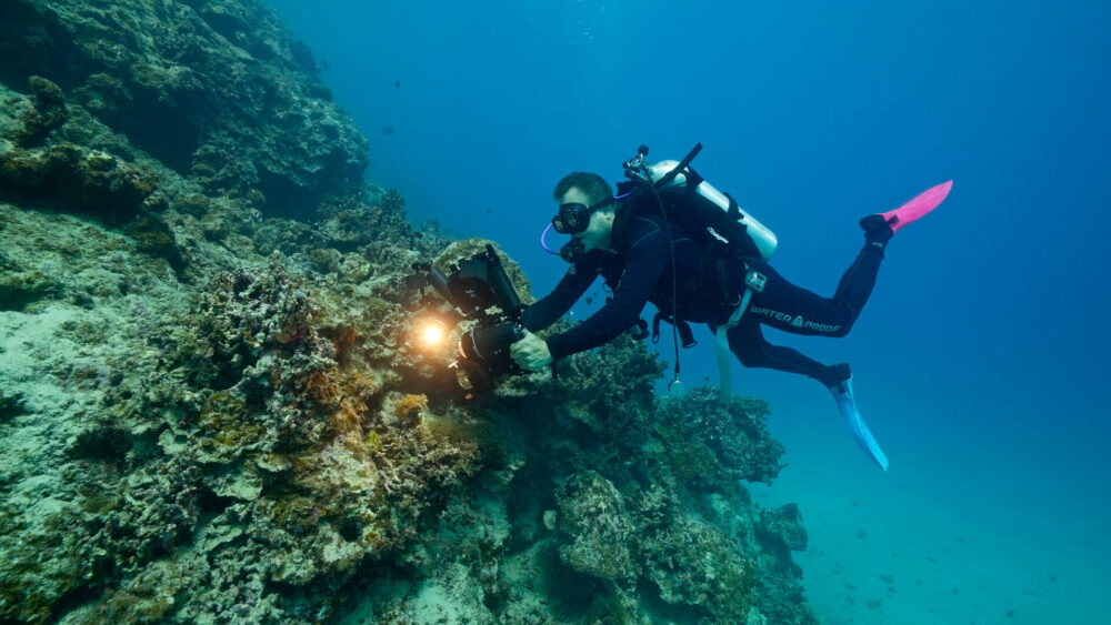 Scuba diver with underwater camera explores coral reef, part of the endless frontier.