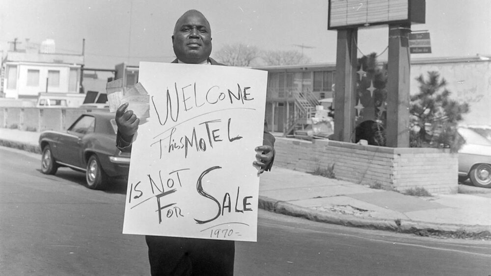 Man holding "Welcome, This Motel is Not For Sale 1970" sign outside Lorraine Motel.