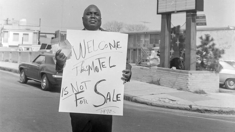 Man holding "Welcome, This Motel is Not For Sale 1970" sign outside Lorraine Motel.