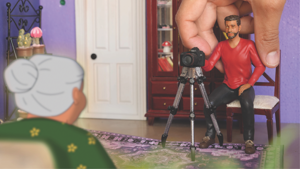 Miniature man with camera in dollhouse, filmed by unseen person.