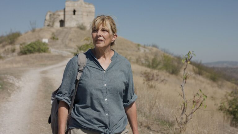Woman with backpack walks on dusty path towards ancient ruins