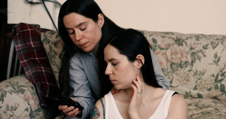 Two women looking at a phone on a floral couch, representing a woman's place is everywhere.