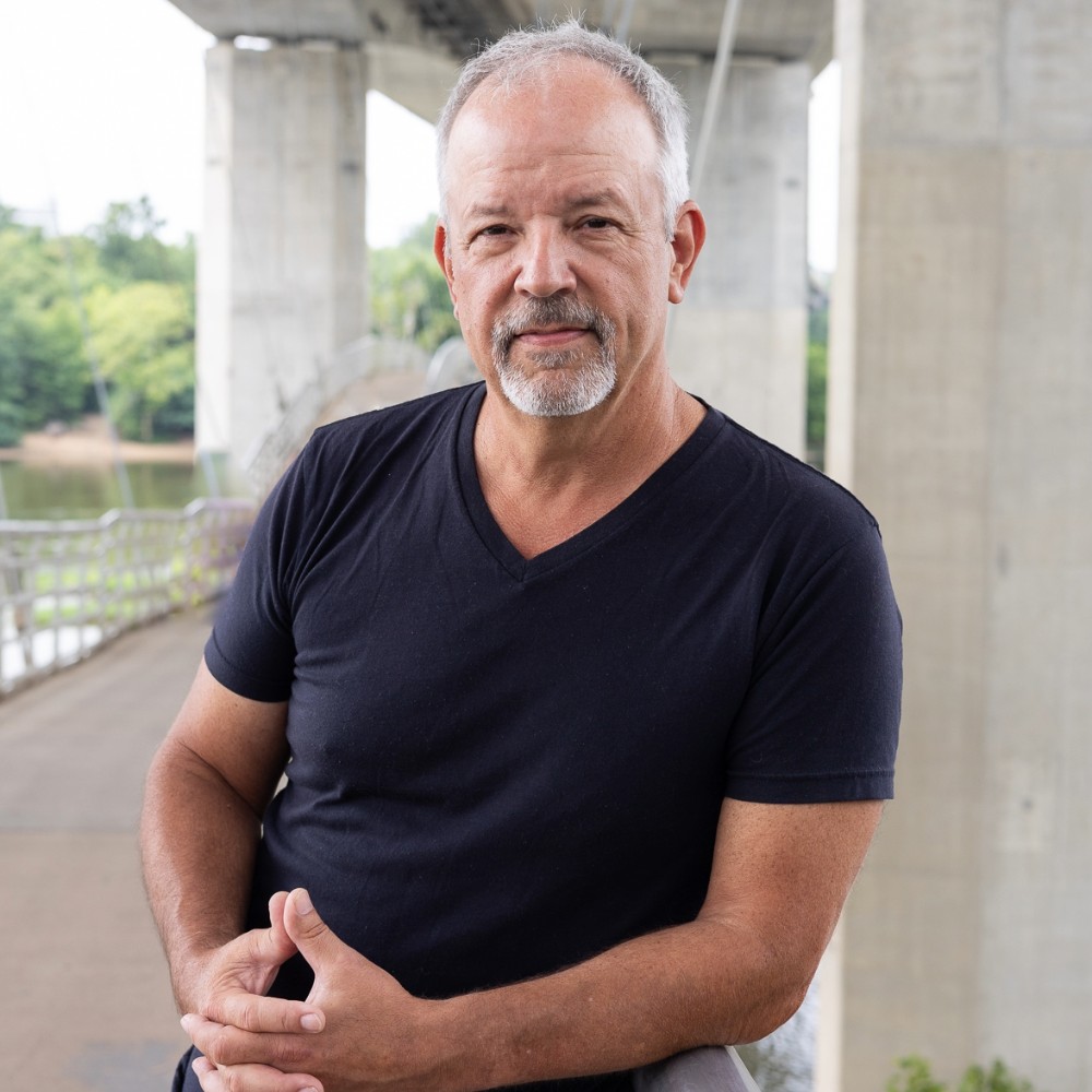 Andy Edmunds, a man with a goatee, leans on a railing under a bridge.