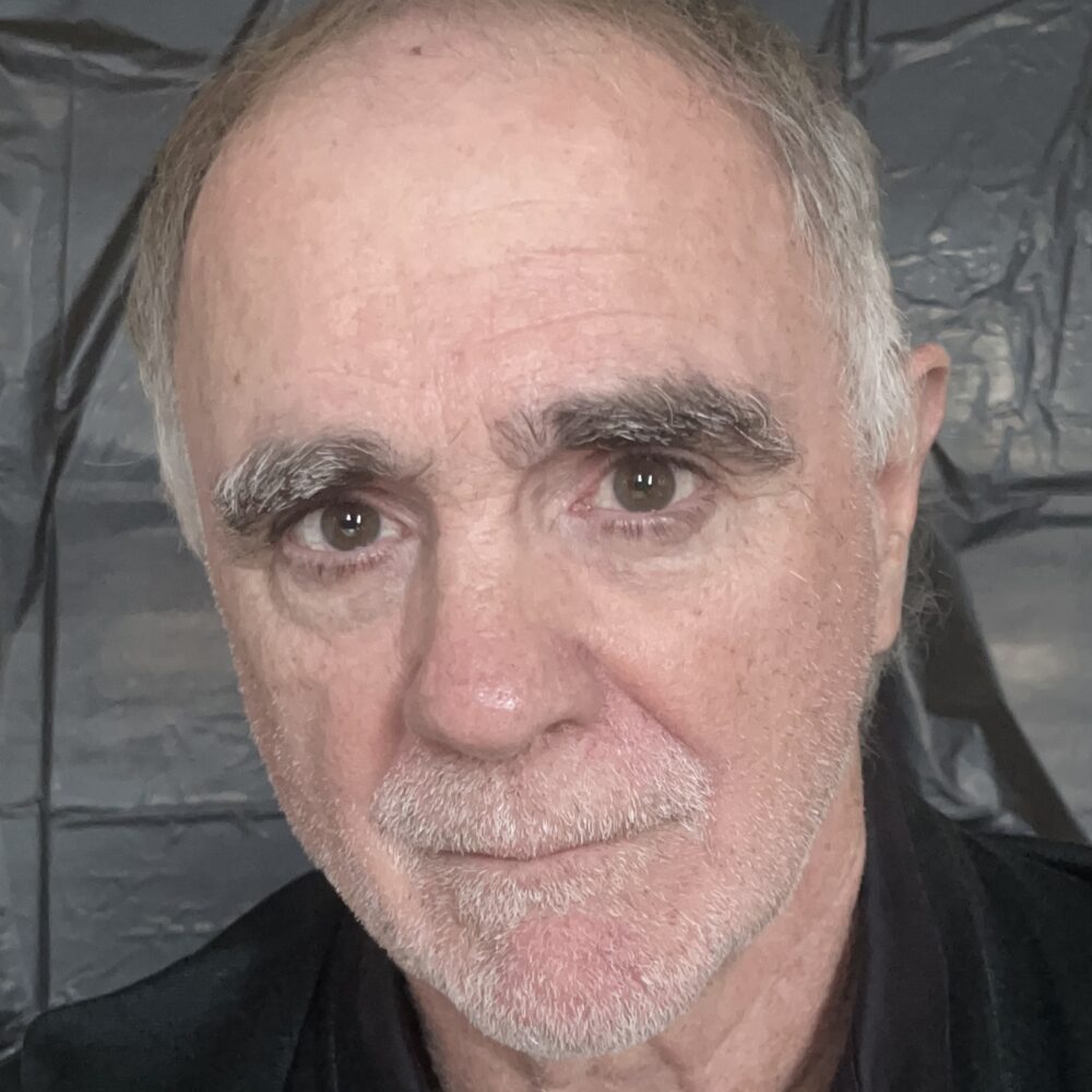 Christopher Spelman, a man with graying hair and prominent eyebrows, looks directly at the camera.