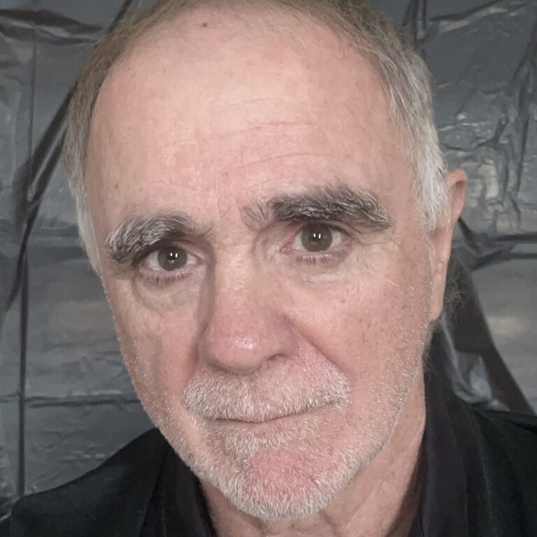 Christopher Spelman, a man with graying hair and prominent eyebrows, looks directly at the camera.