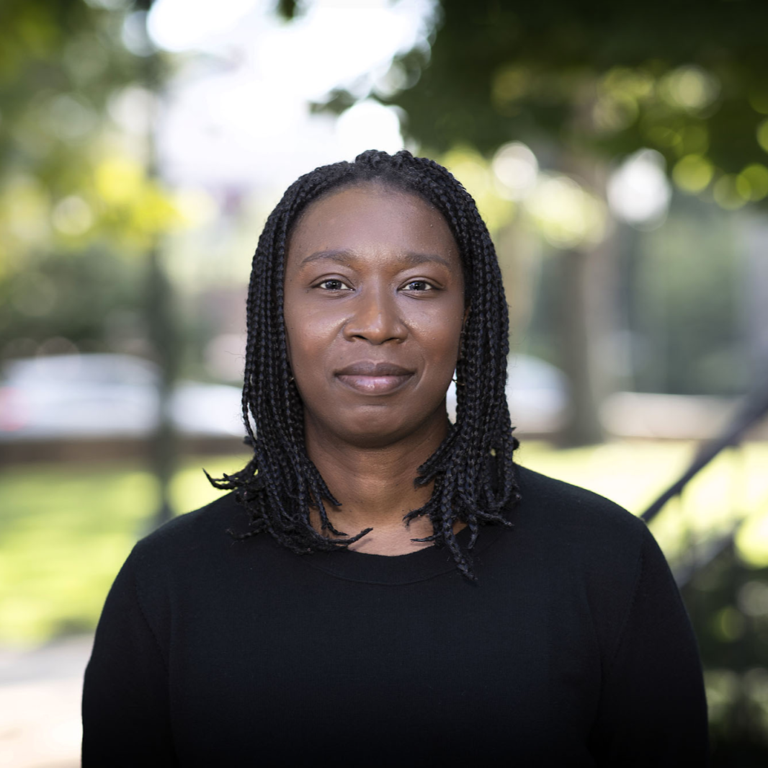 Claudrena Harold, a Black woman with braided hair, smiles at the camera outdoors.