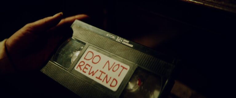 Hand holding VHS tape with "DO NOT REWIND" label