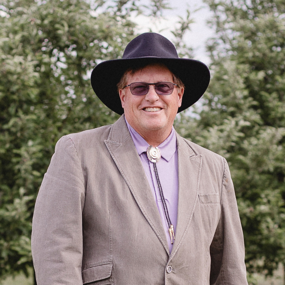 David Gum, a man in a cowboy hat and bolo tie, smiles outdoors.