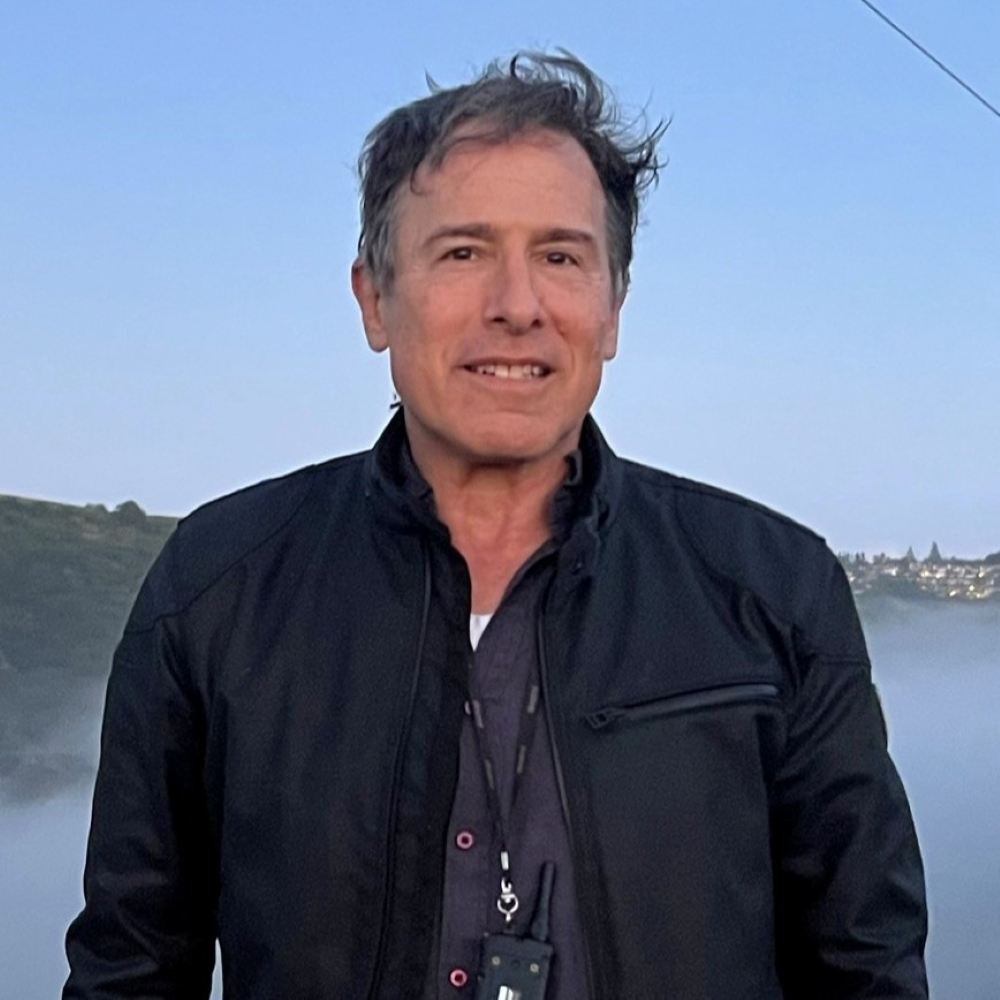 David O. Russell in a black jacket with a misty landscape behind him.
