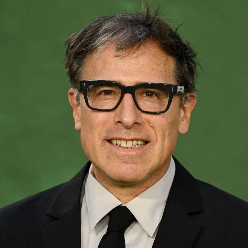 David O. Russell wearing black-rimmed glasses and a suit, smiling