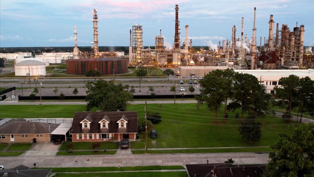 Residential neighborhood borders industrial refinery with towering structures.