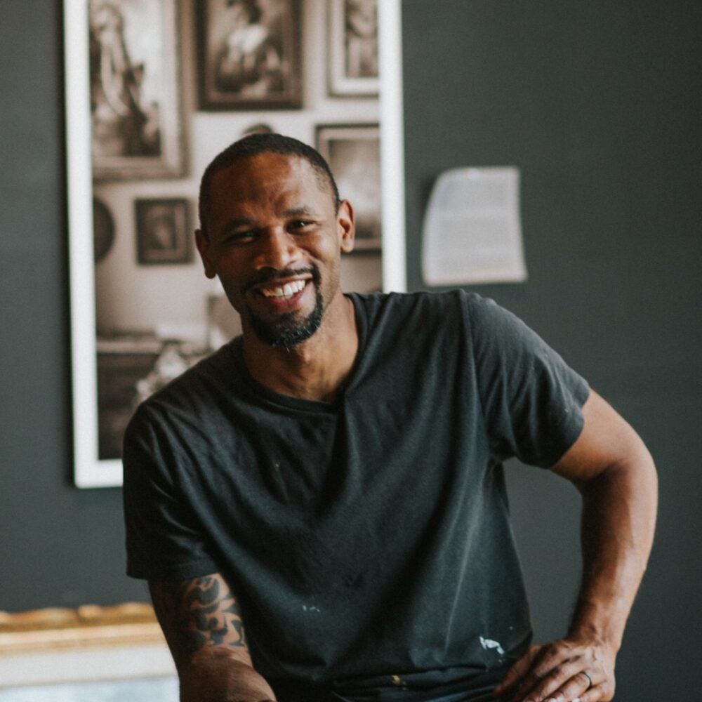Hamilton Glass smiles confidently in his studio, surrounded by framed art.