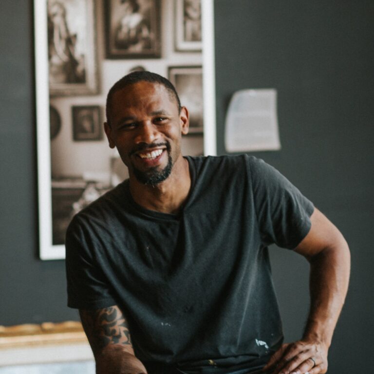 Hamilton Glass smiles confidently in his studio, surrounded by framed art.