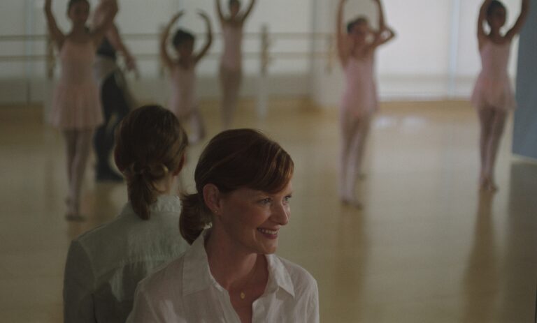Ballet instructor smiles at young dancers practicing in a studio