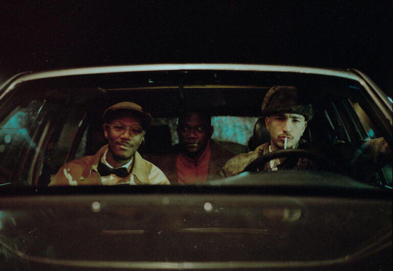 Three men in hats in a car at night, possibly related to JAZZ INFERNAL.