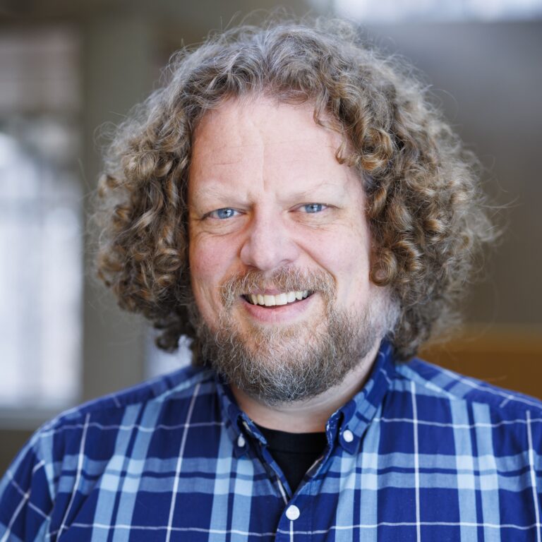 Portrait of Jason Evans Groth, a man with curly hair and a beard wearing a blue plaid shirt.