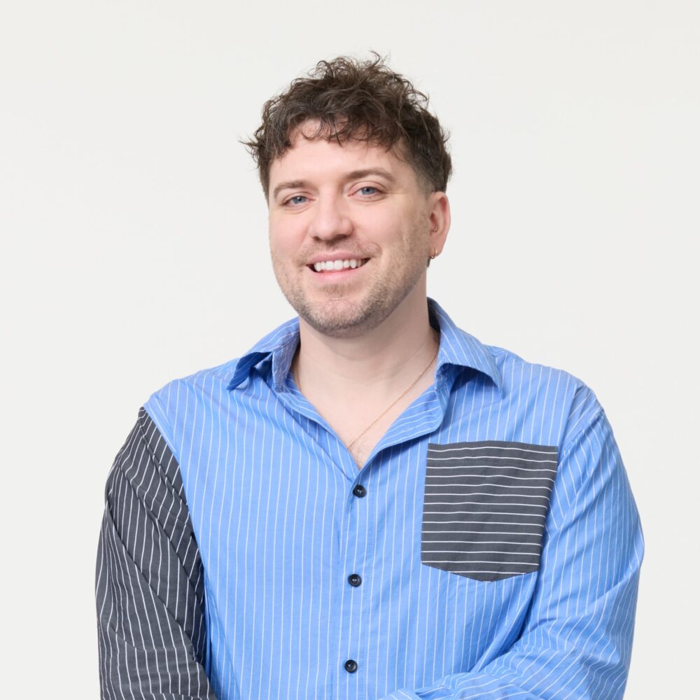 Jason Ikeler, a man with curly brown hair and a blue striped shirt, smiles at the camera.