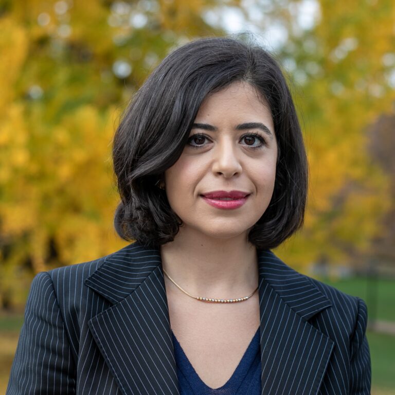 Jülide Etem smiles in a professional portrait with a blurred yellow tree background.