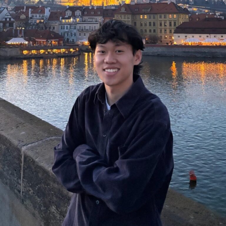 Kenneth Nguyen standing on a bridge in Prague with city lights in the background.