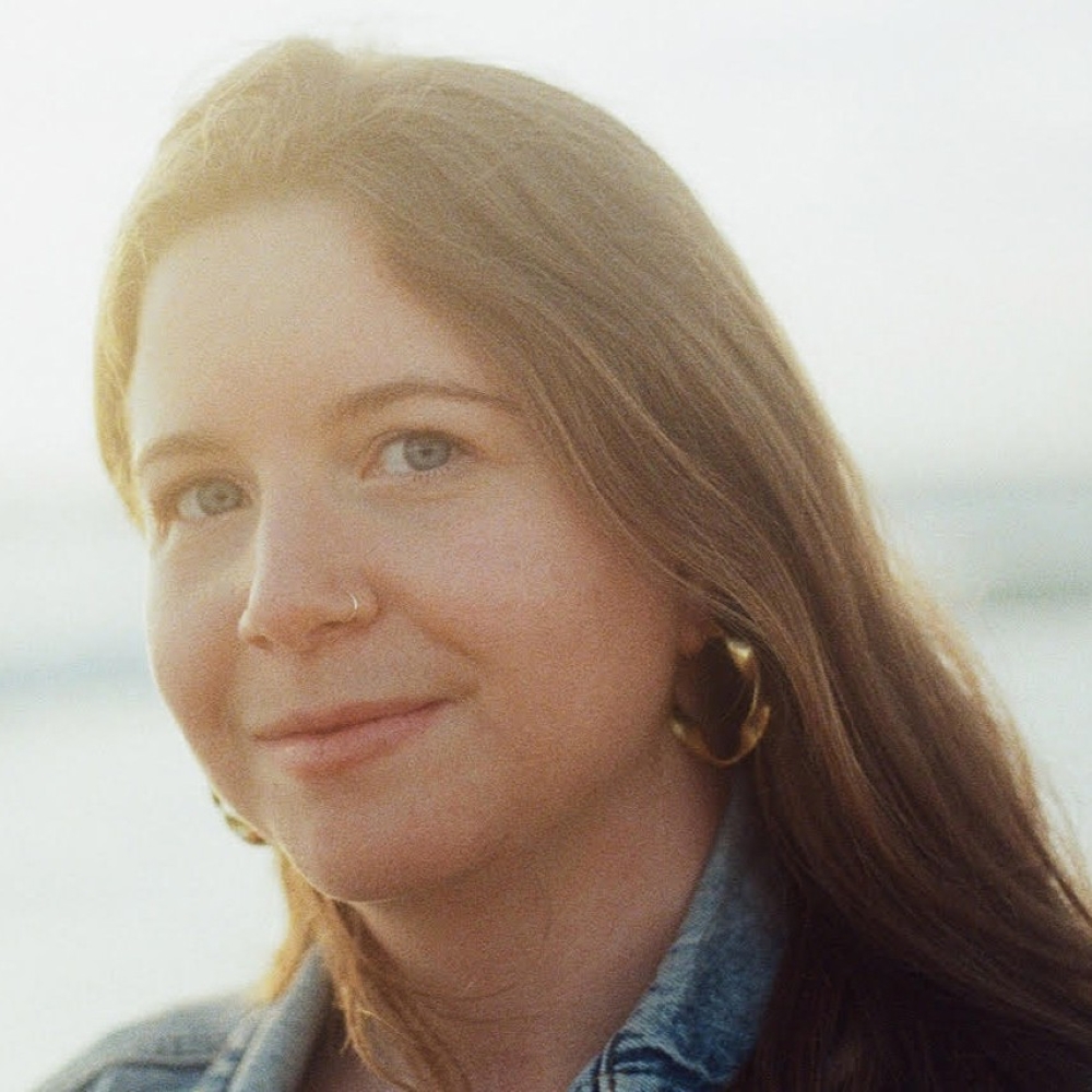 Leah Galant, a young woman with long brown hair and hoop earrings, smiles gently.