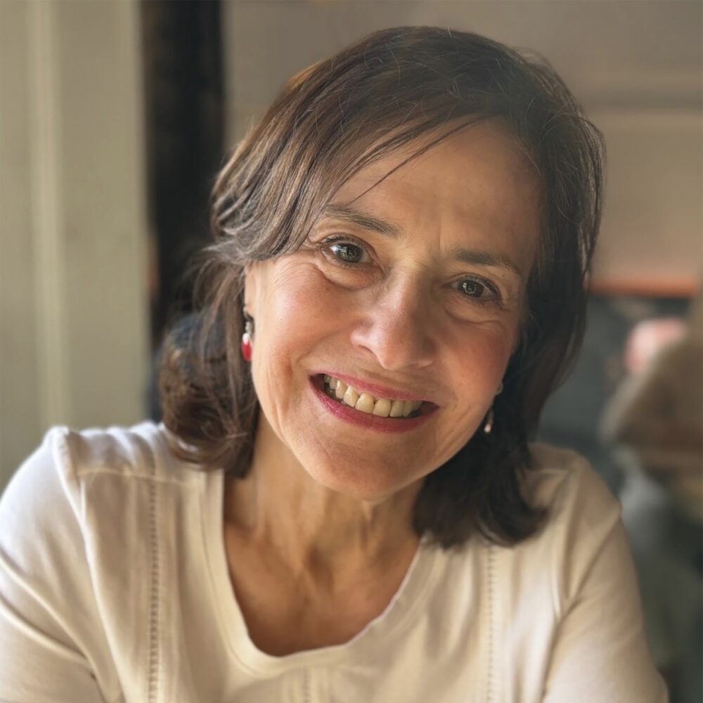 Lisa Stark, a smiling woman with brown hair and red earrings, wearing a white top.