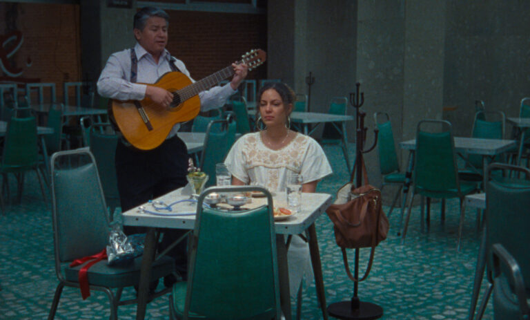 Man plays guitar for woman at table in restaurant