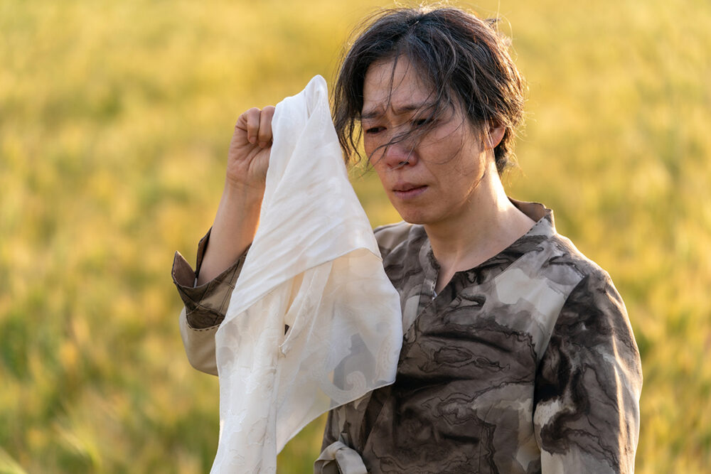 Woman in field, wiping tears with white cloth, from "My Name
