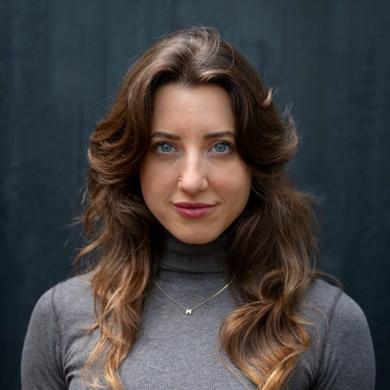 Melissa Lesh, a woman with blue eyes and wavy brown hair, wearing a grey turtleneck.